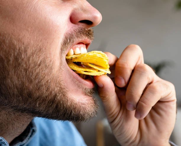 Man eats chips, closeup photo of the eating mouth. Unhealthy eating.